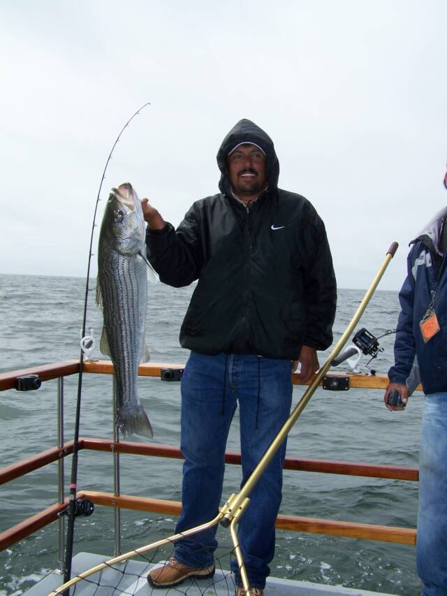 A man in a black nike jacket is holding a large fish