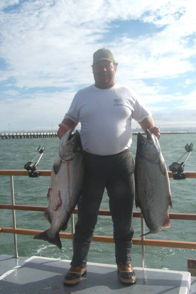 A man is standing on a boat holding two large fish.