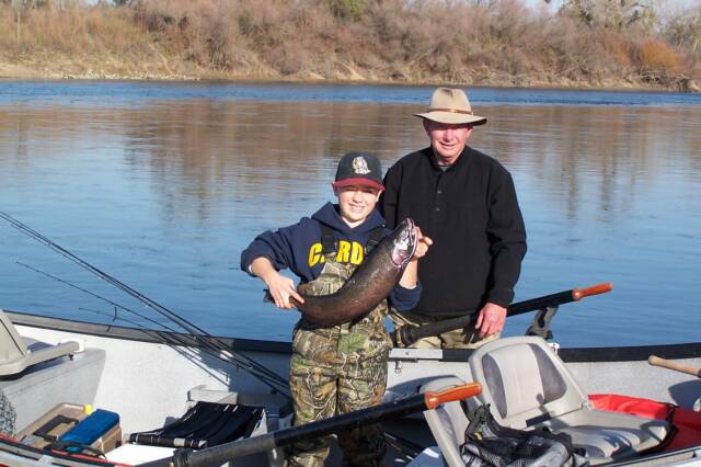 A man and a boy on a boat holding a large fish
