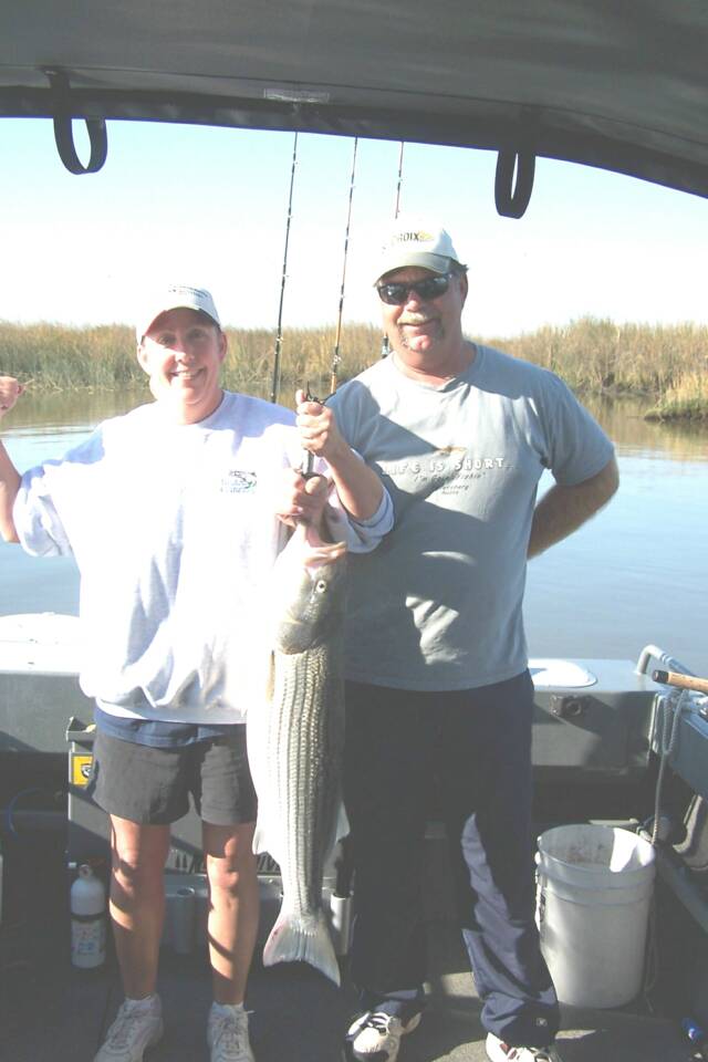 Two men are standing on a boat holding a large fish