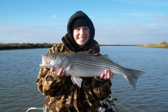 A person is holding a large fish in their hands in front of a body of water.