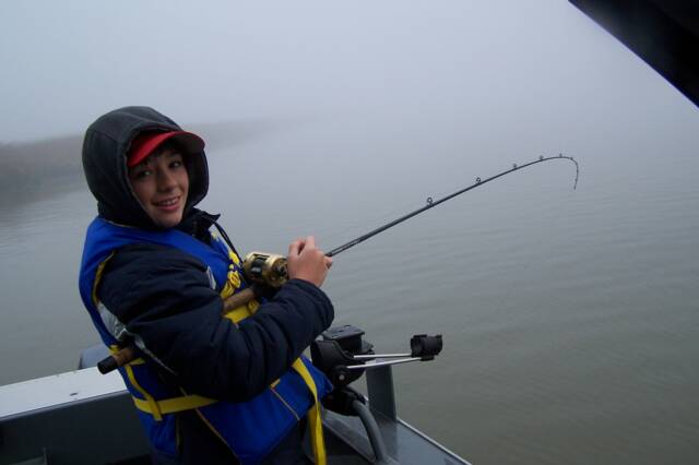 A young boy is fishing on a boat on a foggy day