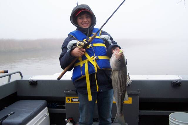 A boy holding a fishing rod and a fish on a boat