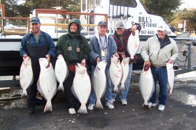 A group of men holding large fish in front of a bill 's fishing boat
