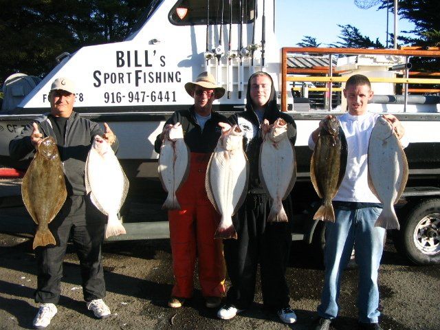 Four men holding fish in front of a bill 's sport fishing boat