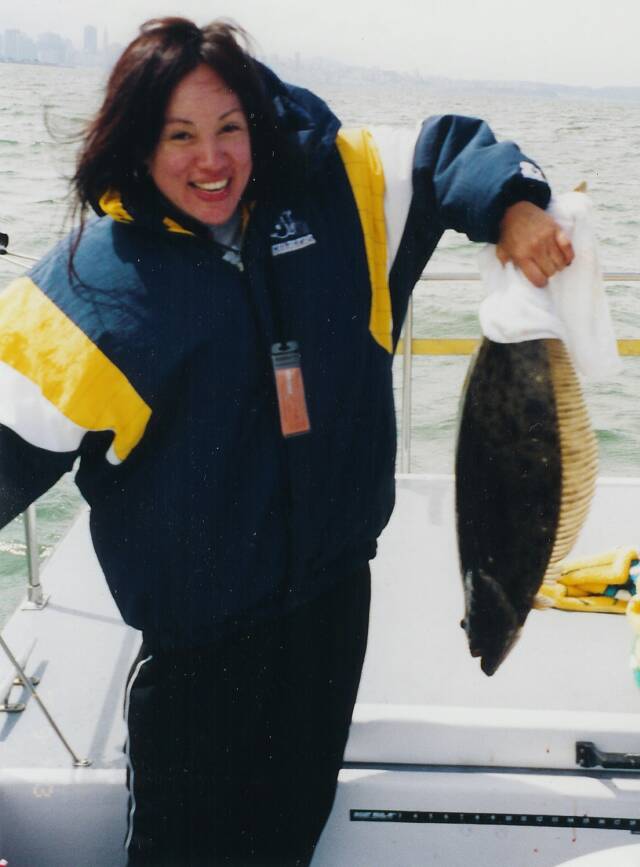 A woman in a blue and yellow jacket is holding a large fish
