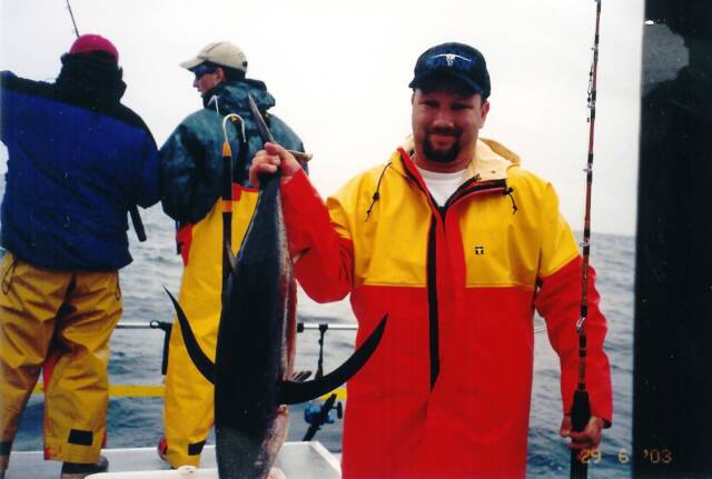 A man in a red and yellow jacket is holding a large fish