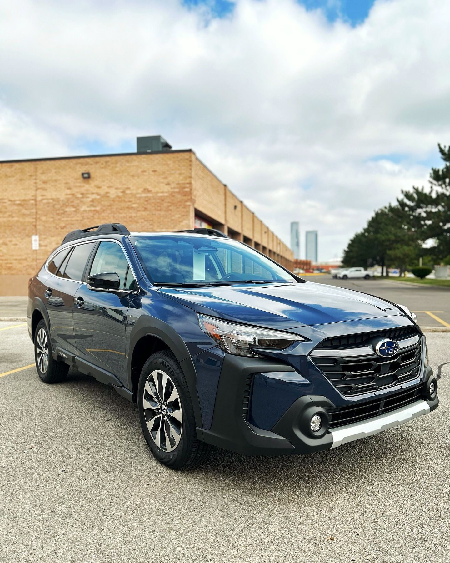 A blue subaru outback is parked in a parking lot in front of a brick building.