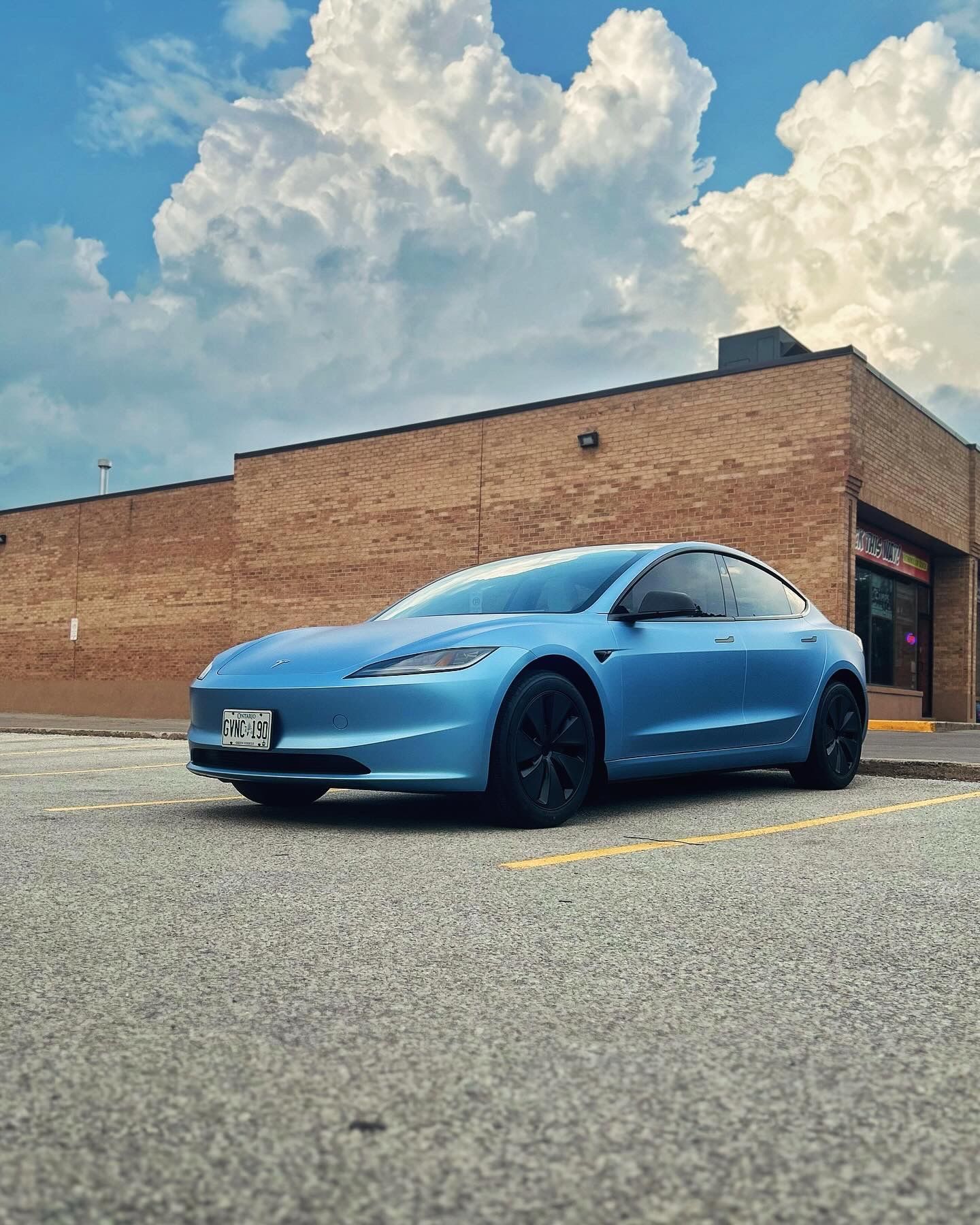 A blue tesla model 3 is parked in front of a brick building.