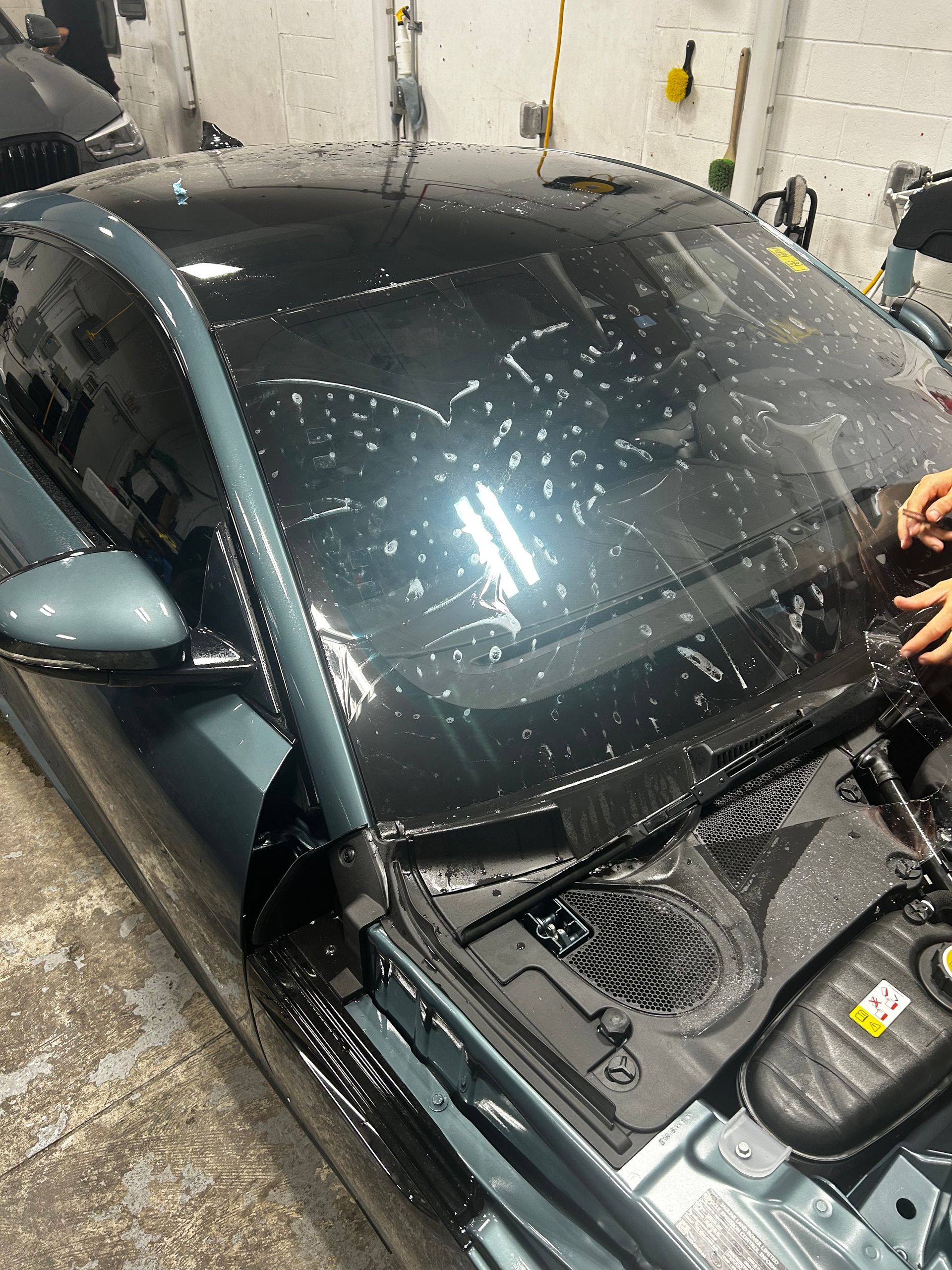 A person is cleaning the windshield of a car in a garage.