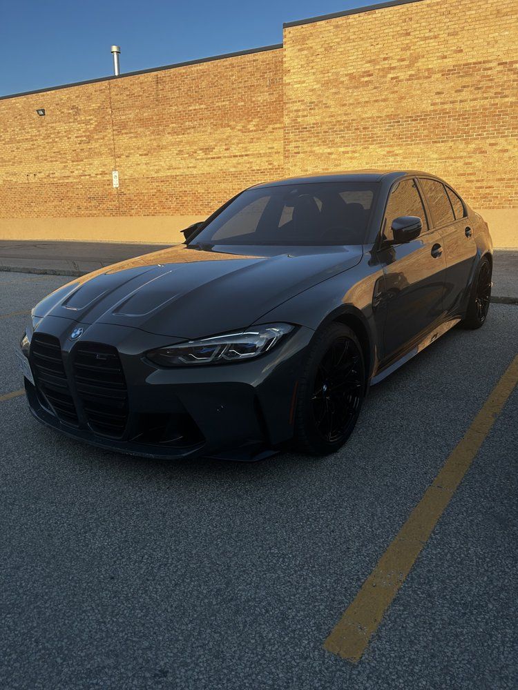 A black bmw is parked in a parking lot in front of a brick building.