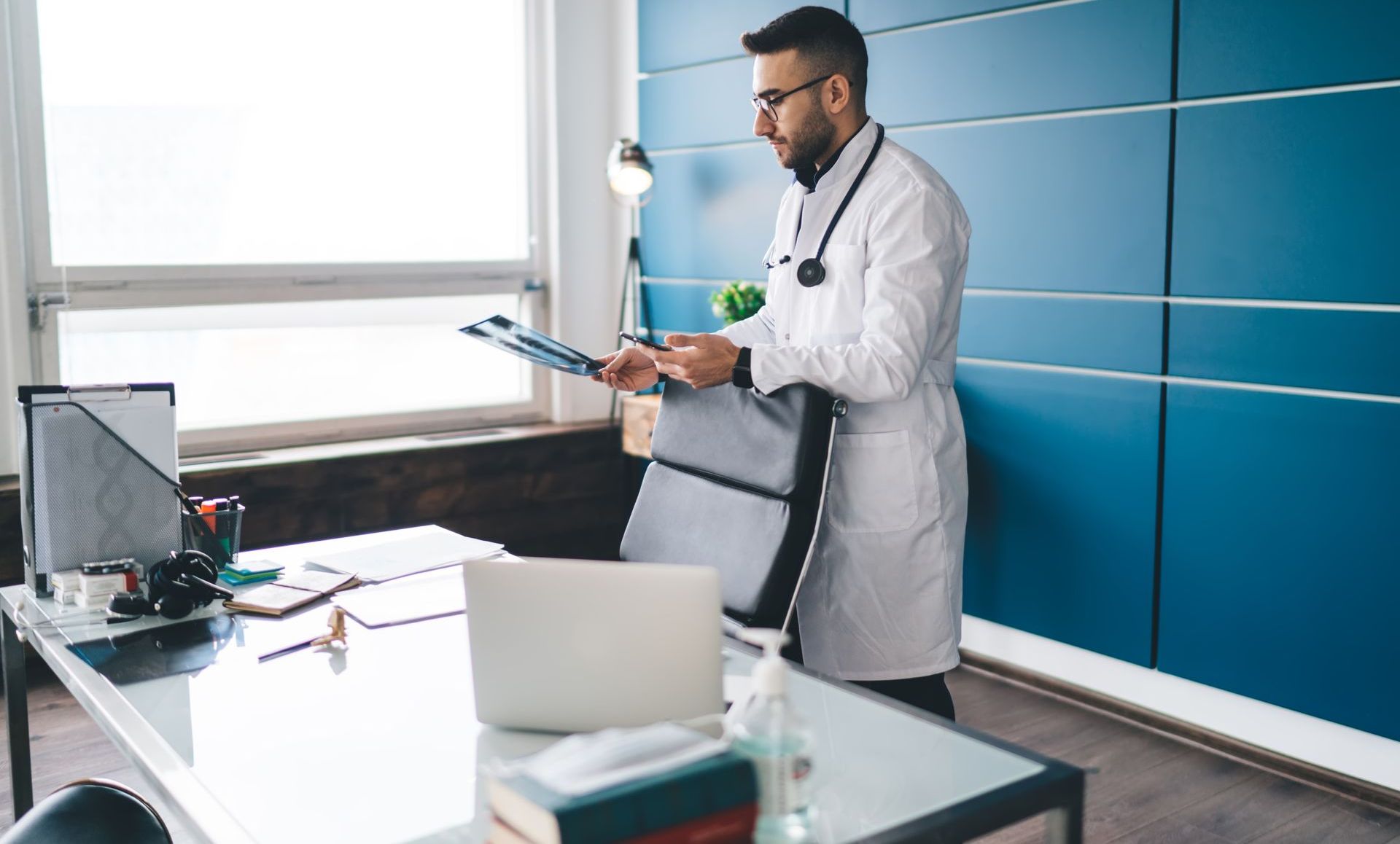A doctor is standing in an office looking at a clipboard.