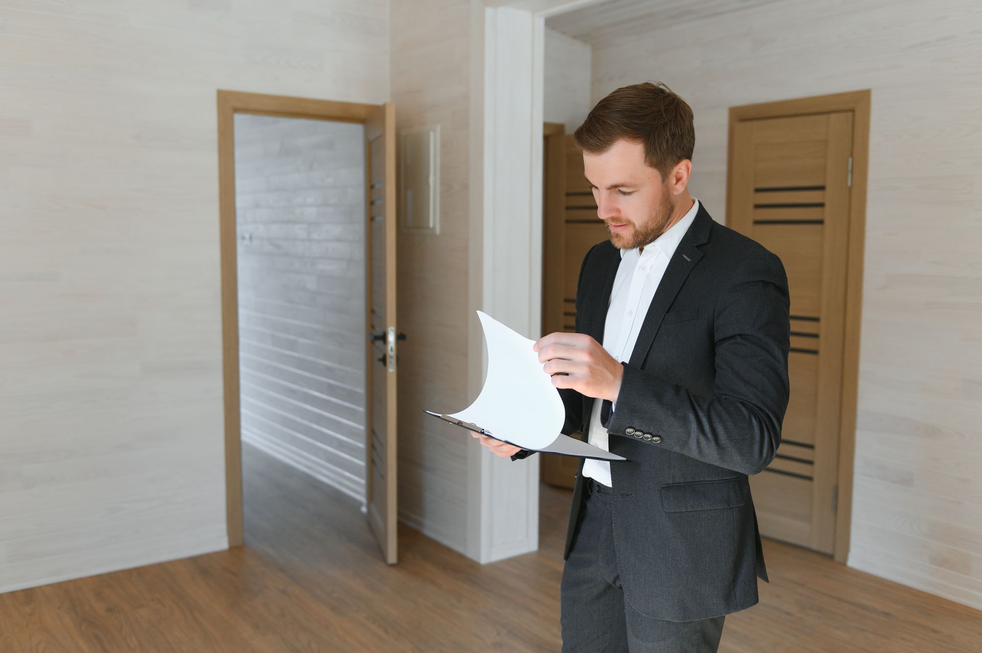 A man in a suit is looking at a piece of paper in an empty room.