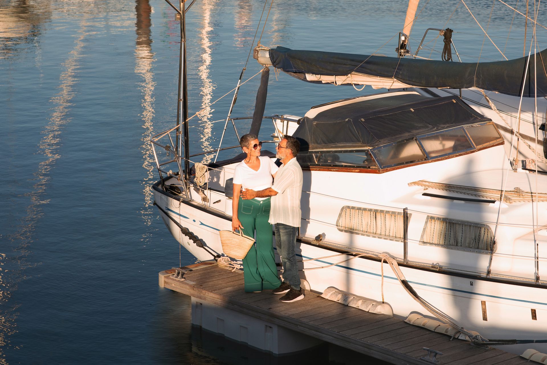 A man and a woman are standing on a dock next to a sailboat.