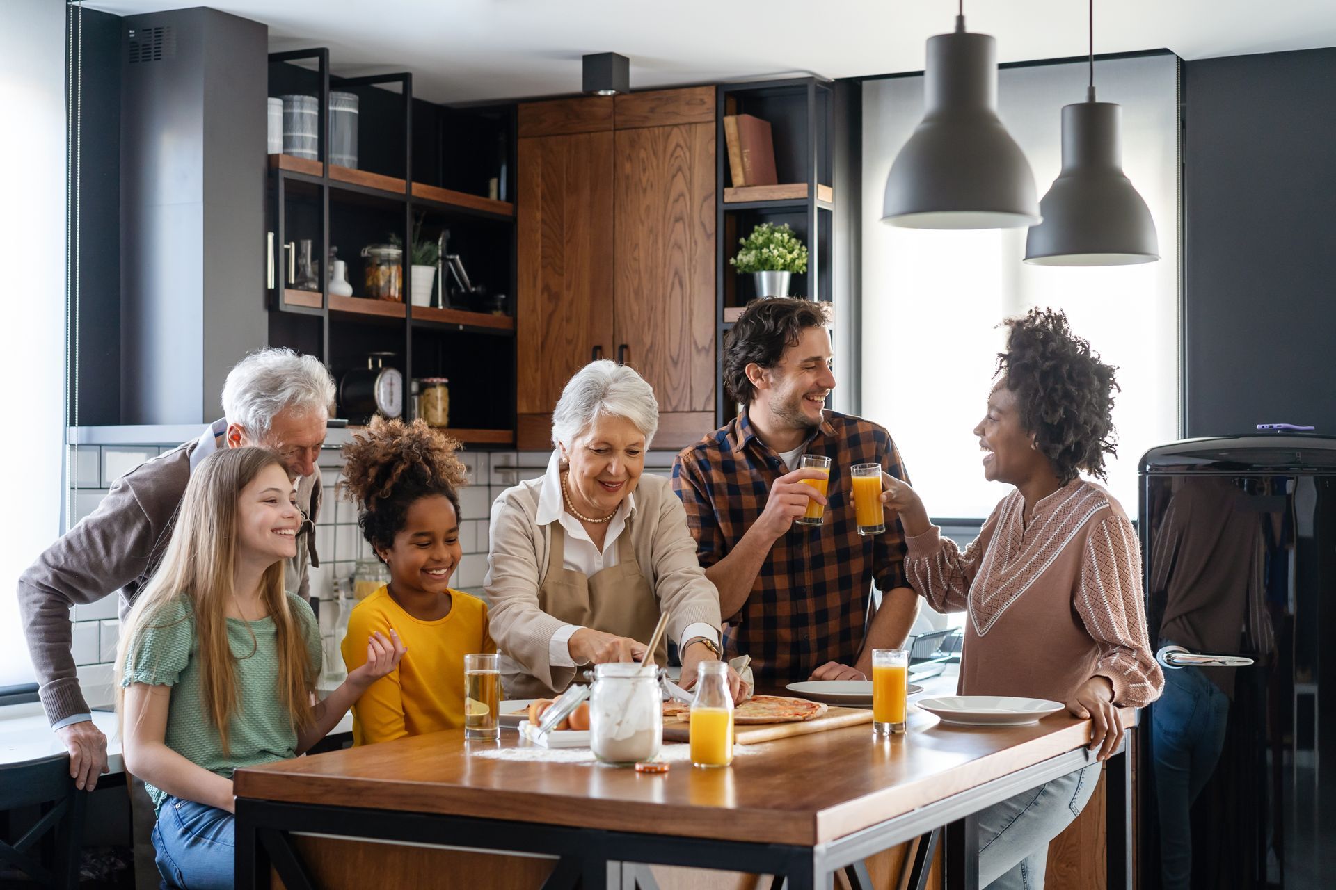 A family is sitting at a table in a kitchen drinking orange juice.