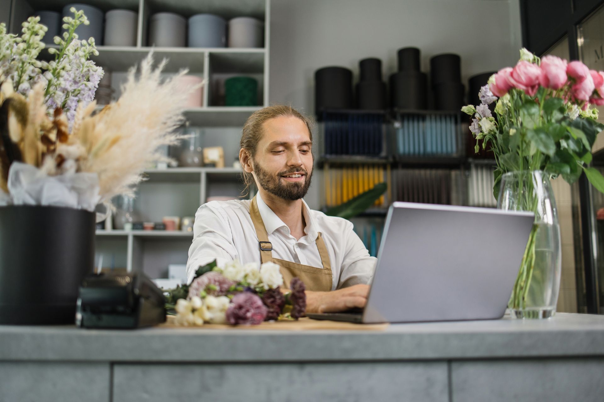 A man is sitting at a counter in a flower shop using a laptop computer.