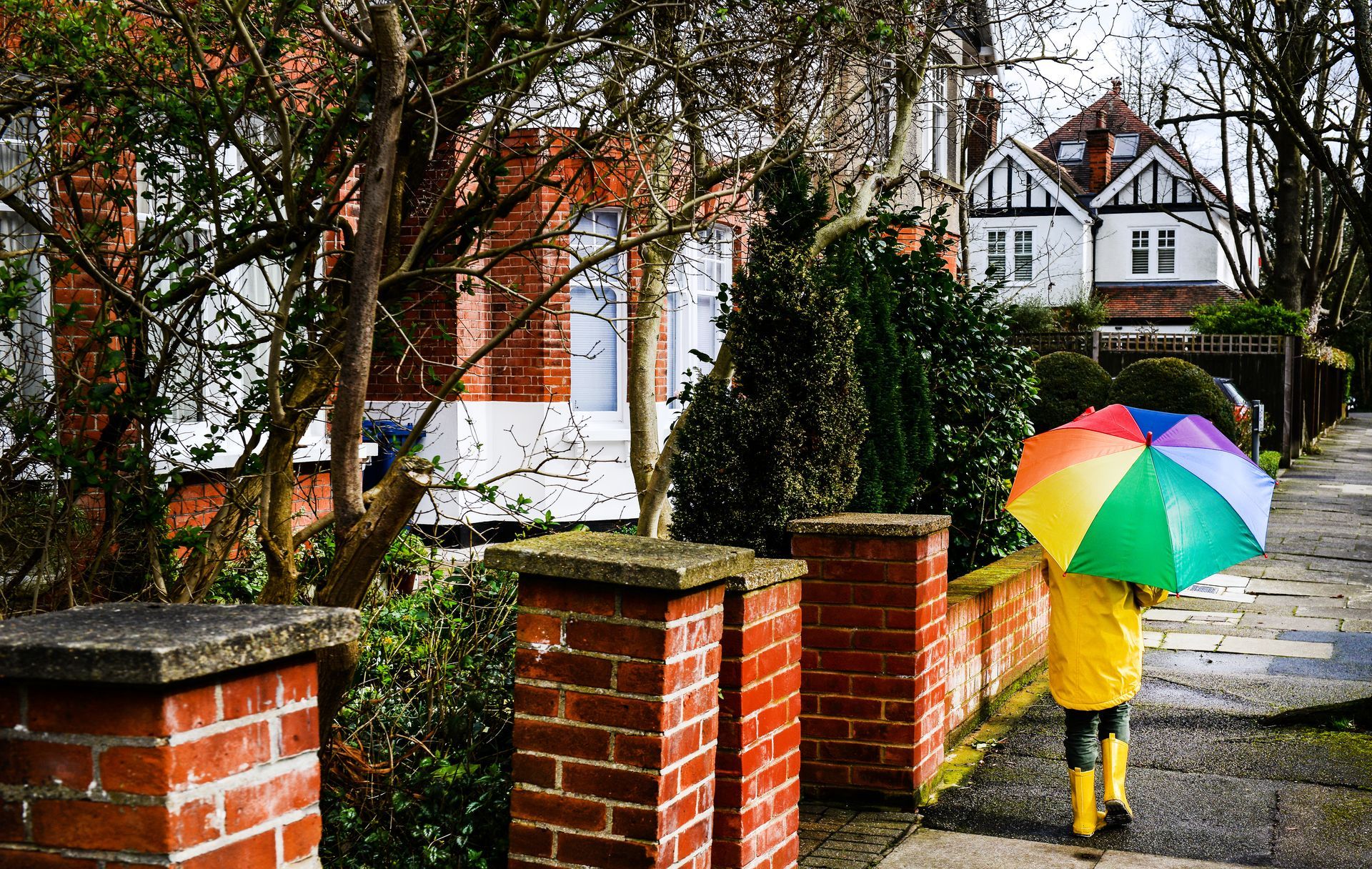 A child is holding a colorful umbrella while walking down a sidewalk.