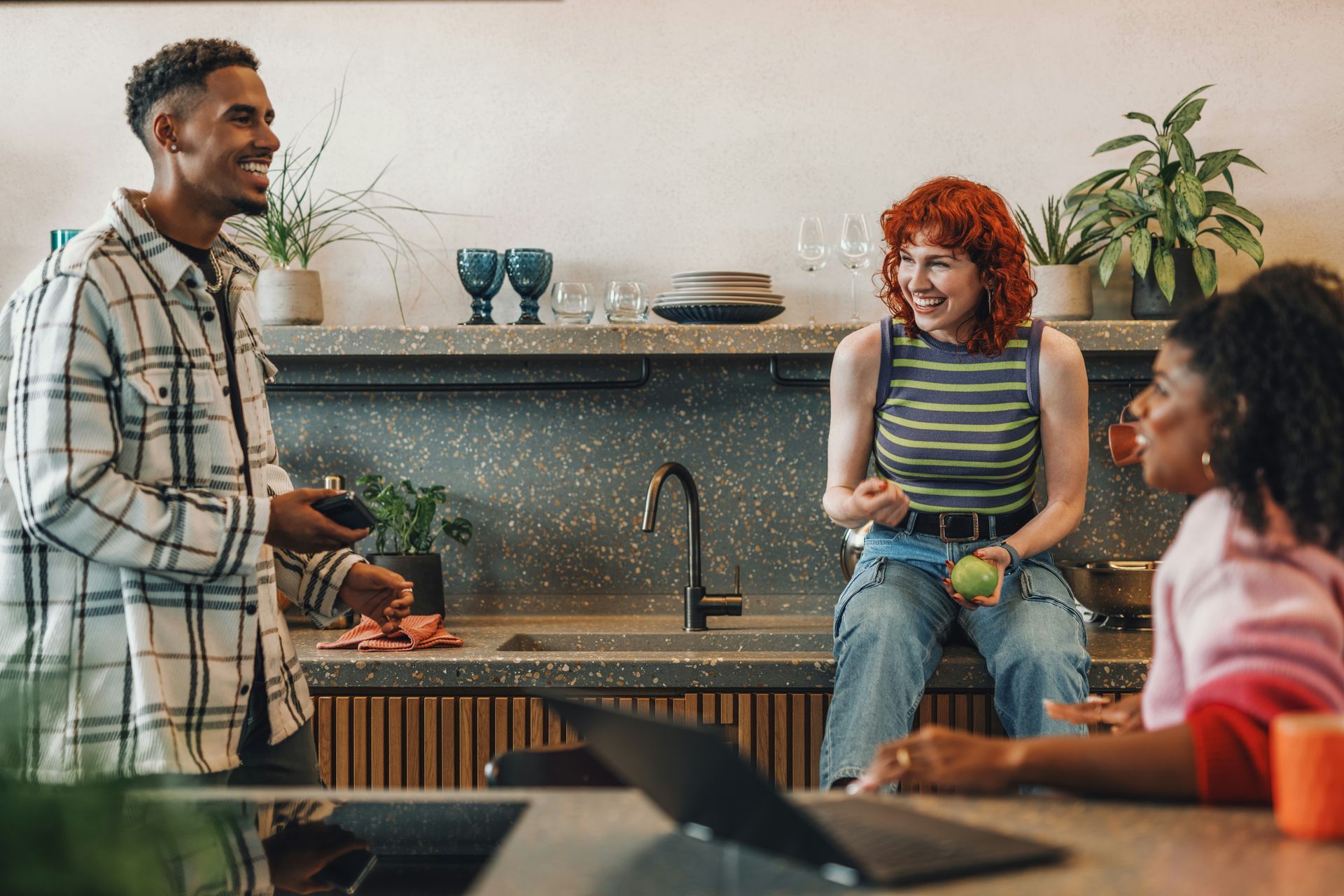 A group of people are sitting at a table in a kitchen talking to each other.