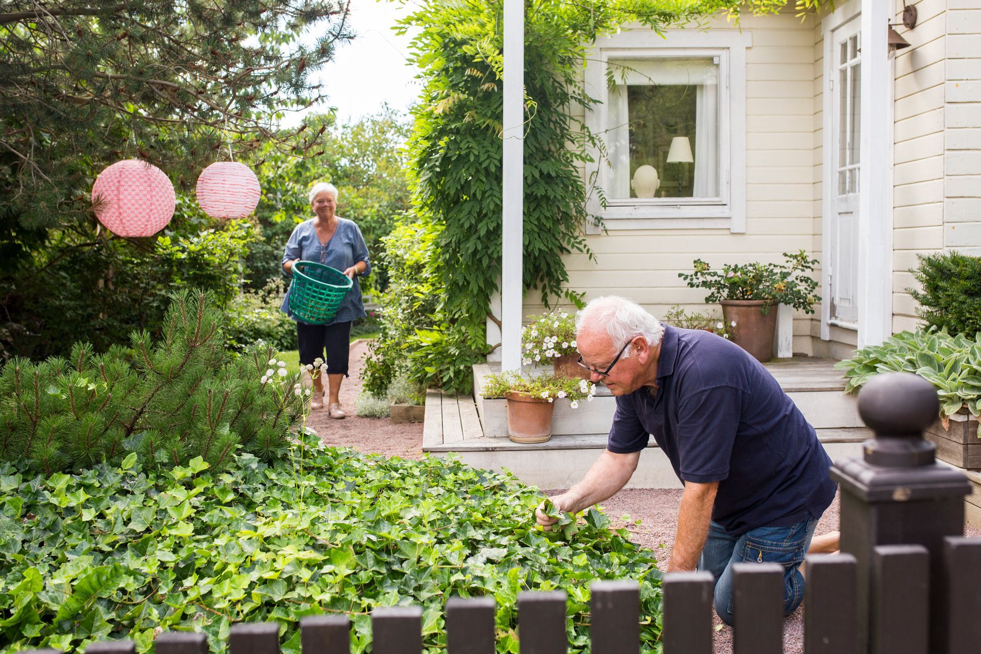 A man and a woman are working in a garden in front of a house.