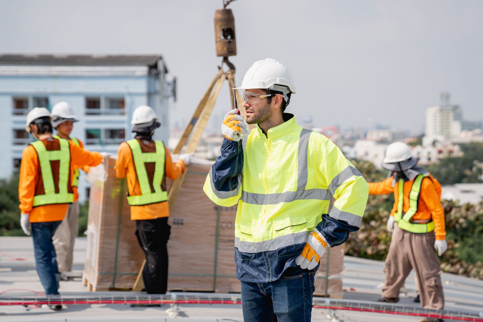 A construction worker is talking on a cell phone while standing next to a crane.