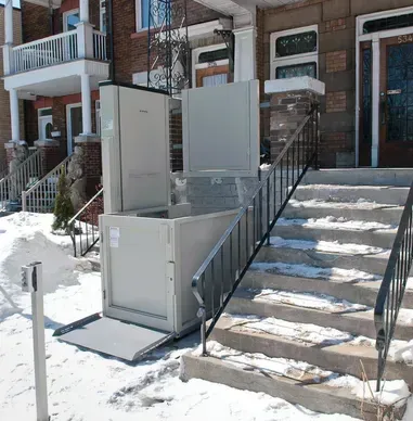 A stair lift is sitting outside of a house in the snow.