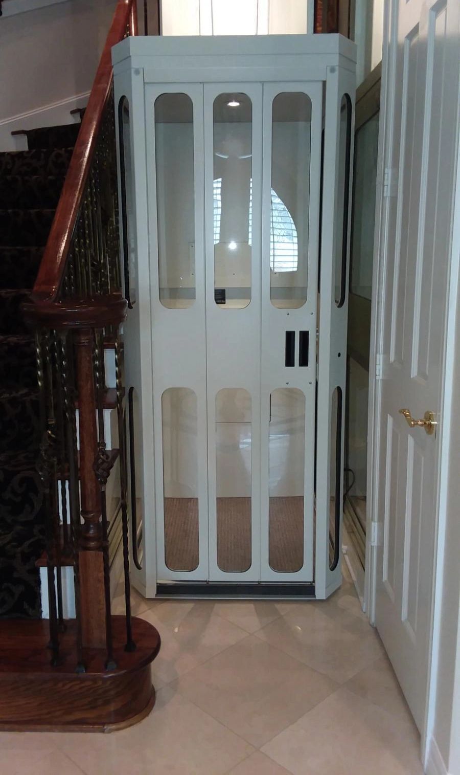 A white elevator is in the middle of a hallway next to a staircase.