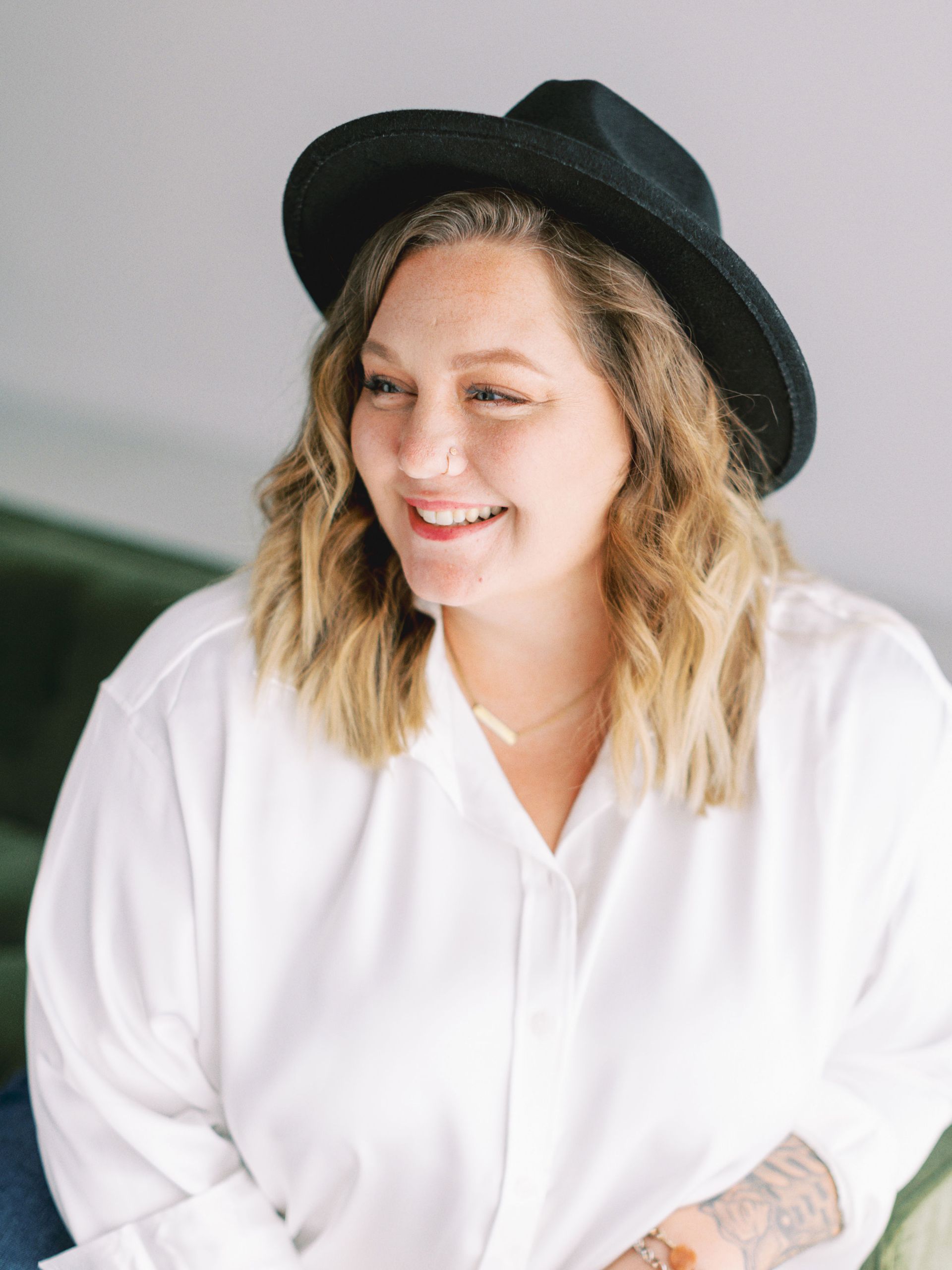 A woman wearing a black hat and a white shirt is smiling.