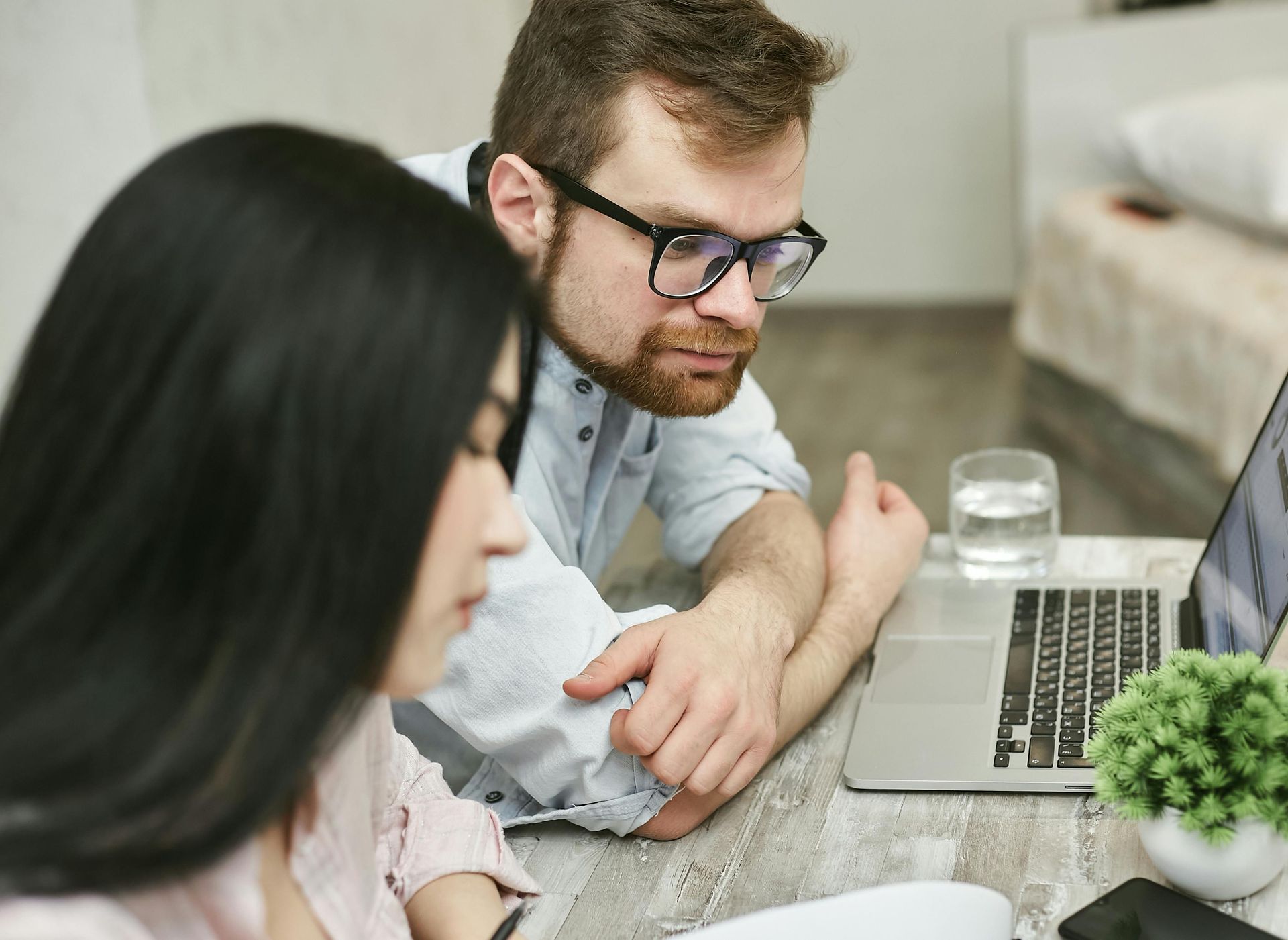 A man and a woman are sitting at a table looking at a laptop.