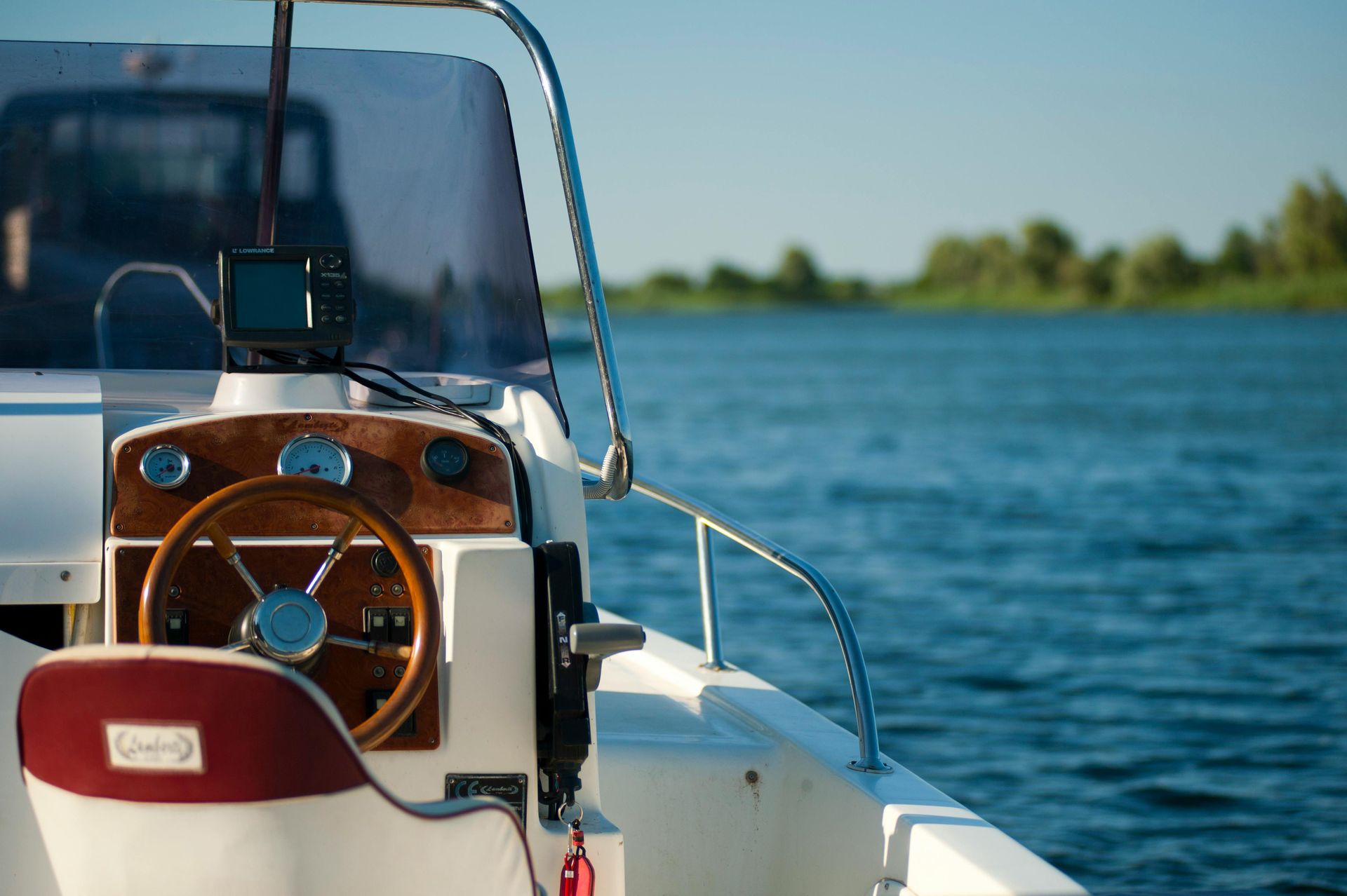 Boat dashboard with wooden steering wheel, seat, and water in background.