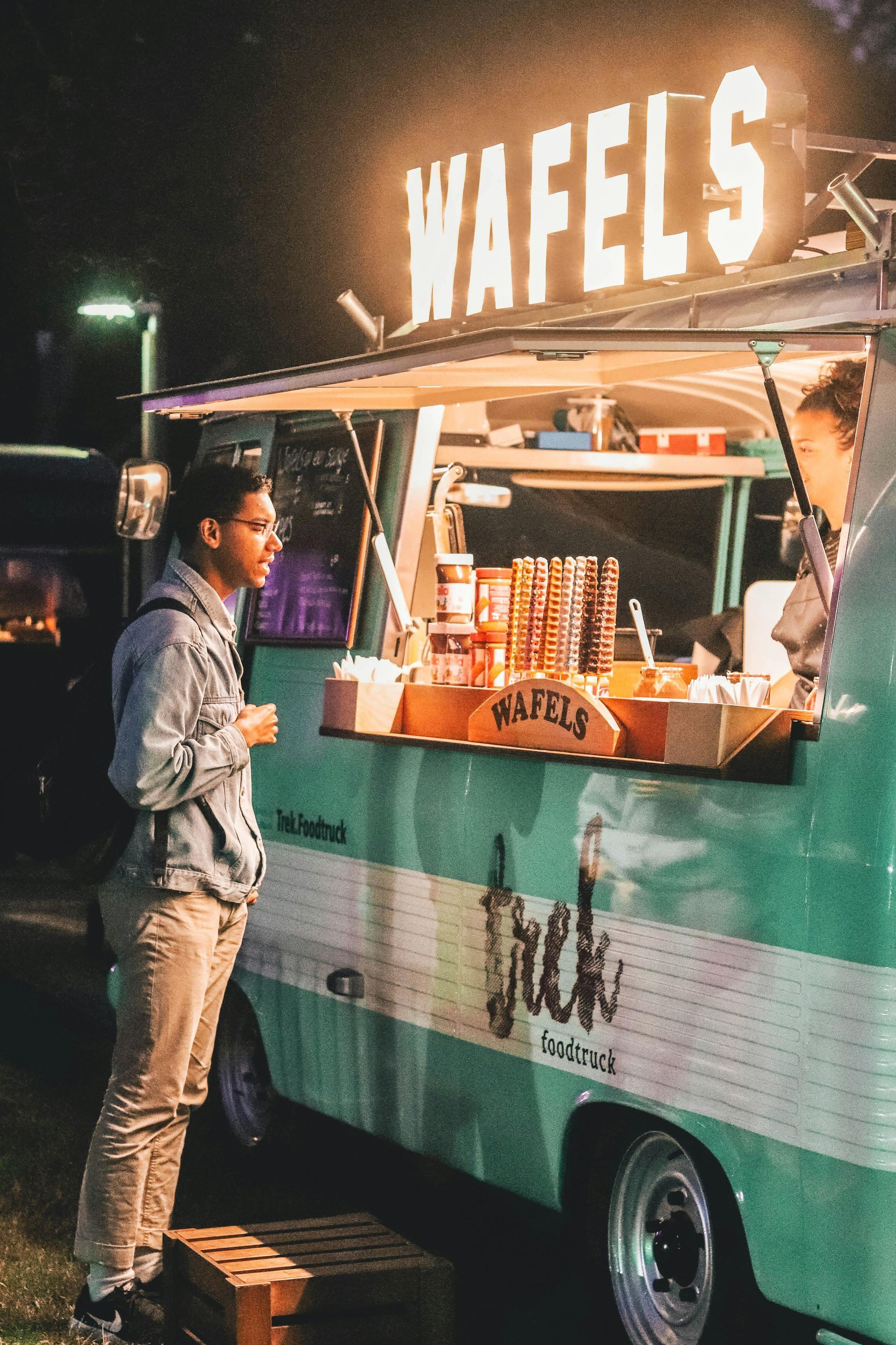 A man is standing in front of a food truck that sells wafels.