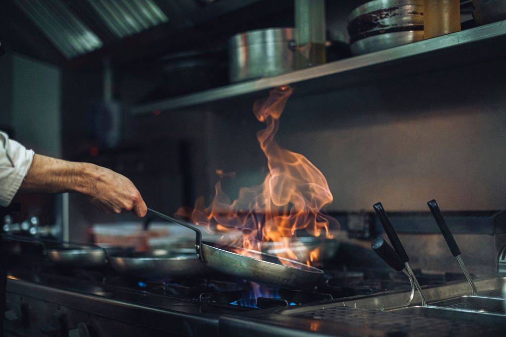 Uno chef sta cucinando del cibo in una padella sul fornello di una cucina.