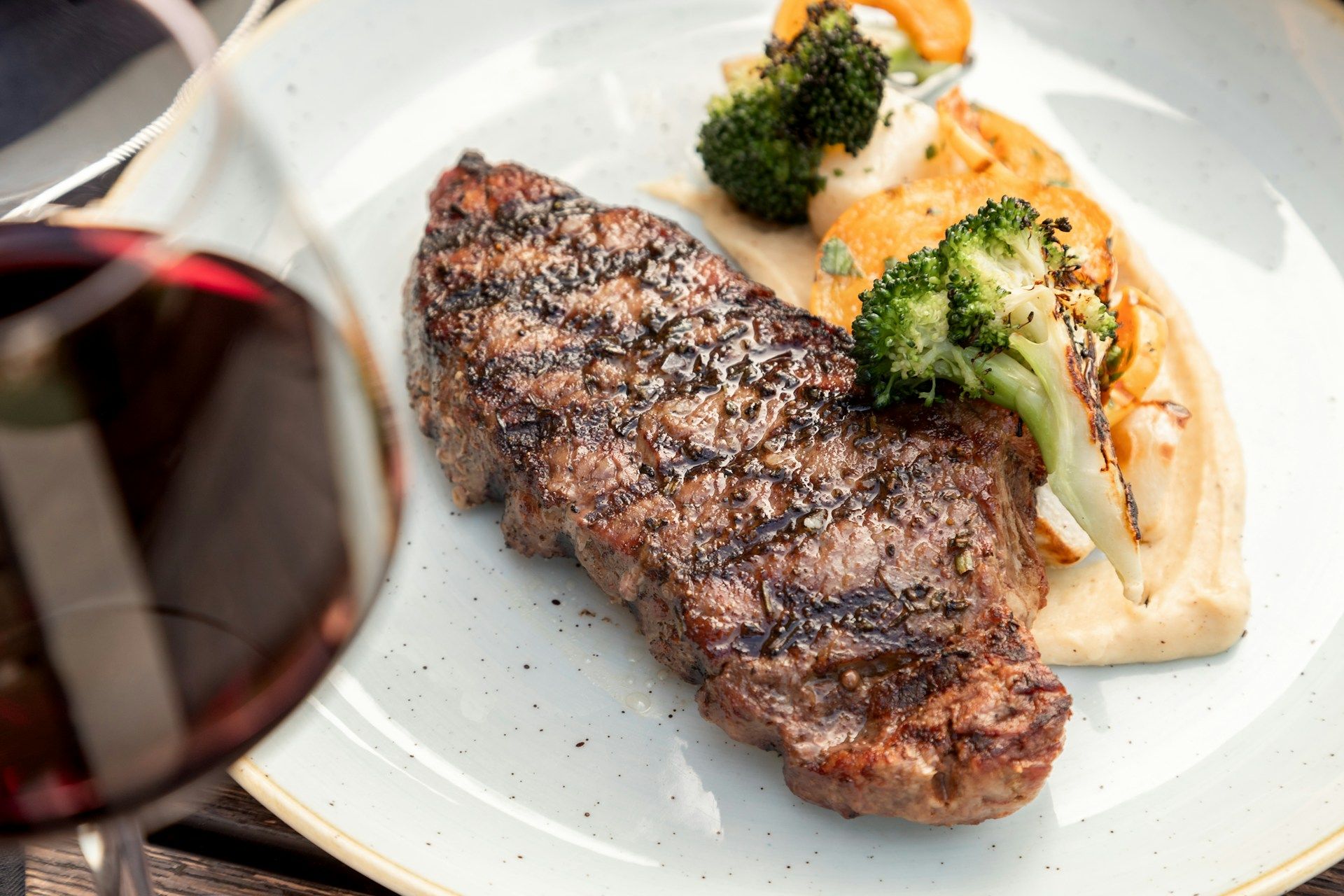a steak and broccoli on a plate next to a glass of wine .