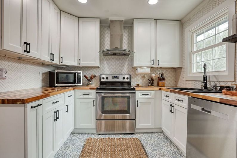 White kitchen with stainless steel appliances, butcher block countertops, and mosaic backsplash.