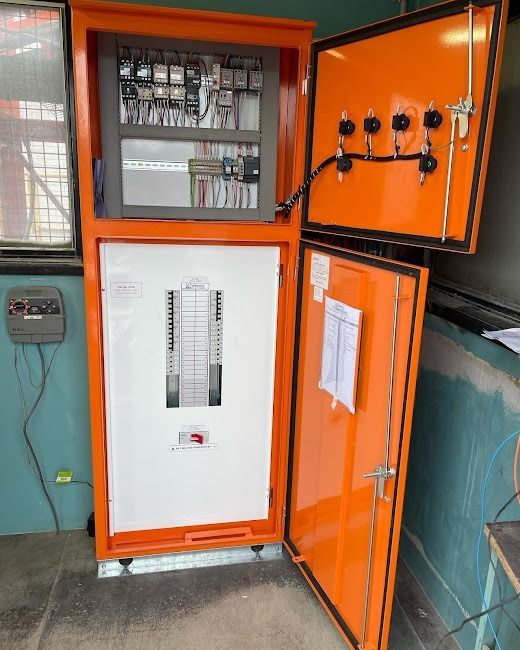 An orange electrical control panel stands open in a room, revealing circuit breakers, wiring, and wall-mounted controls.