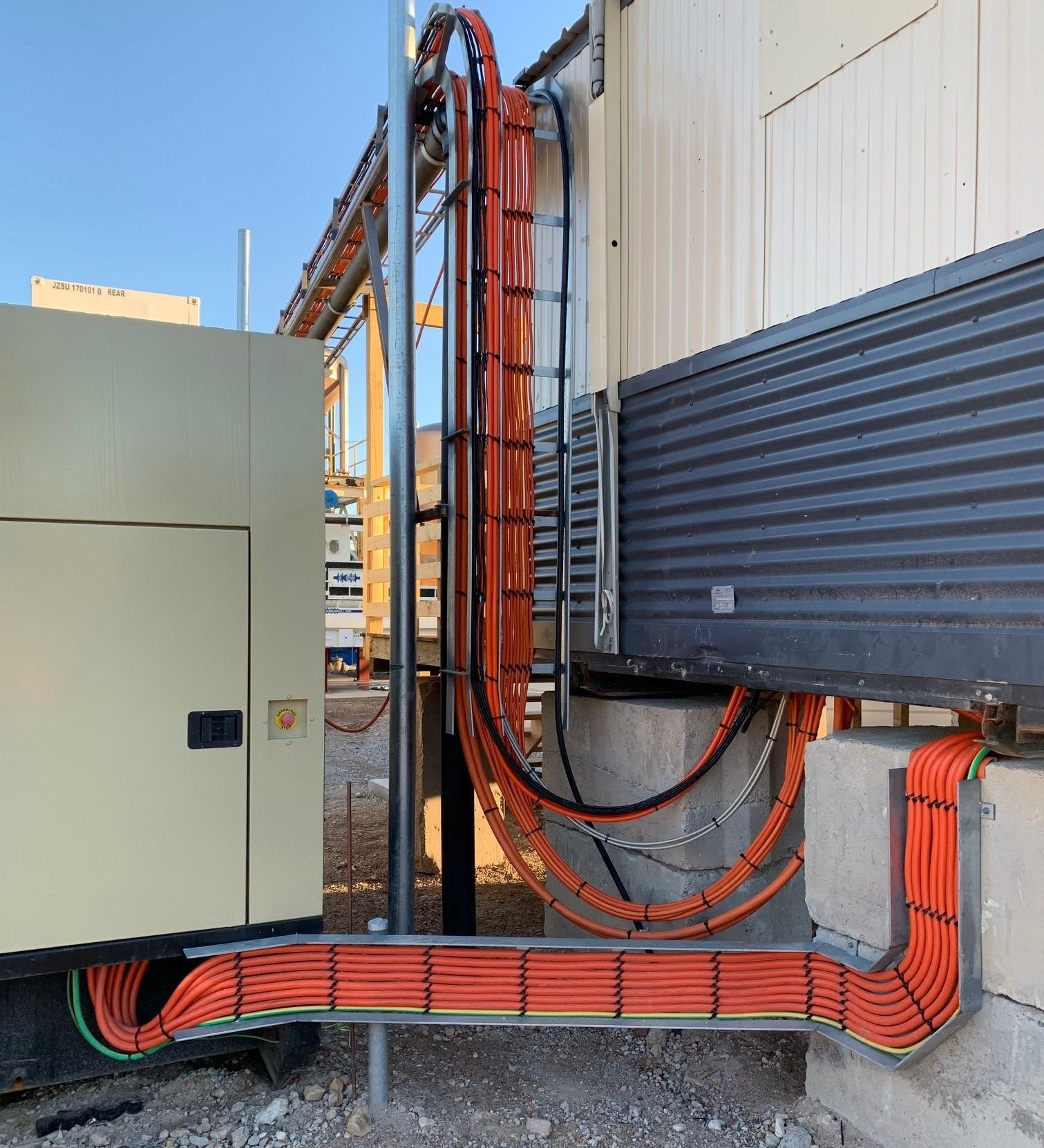 Bright orange electrical cables neatly routed through metal trays connecting a generator to a building exterior.