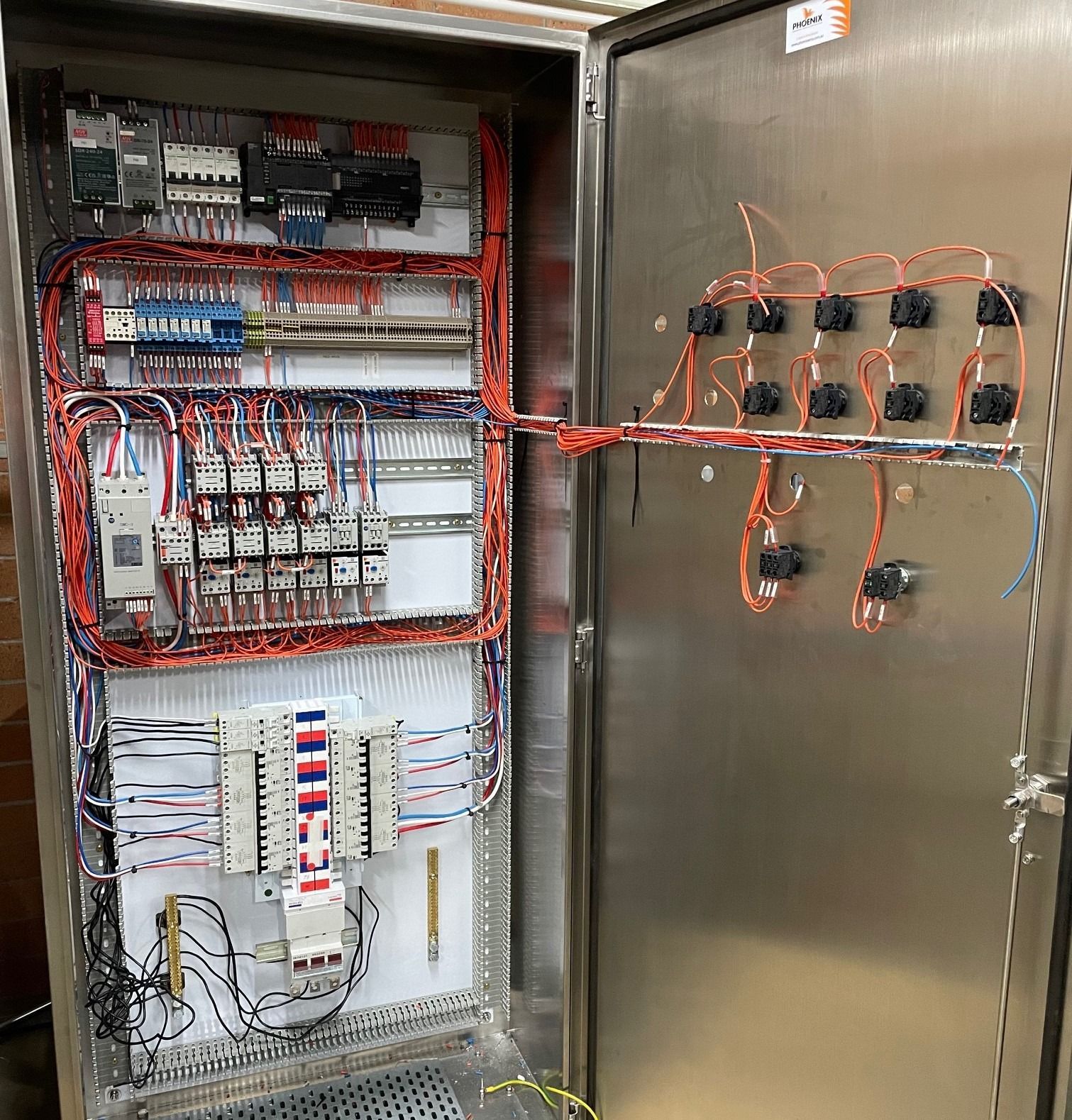 An open electrical control cabinet featuring organized, color-coded wiring, terminal blocks, and mounted components.