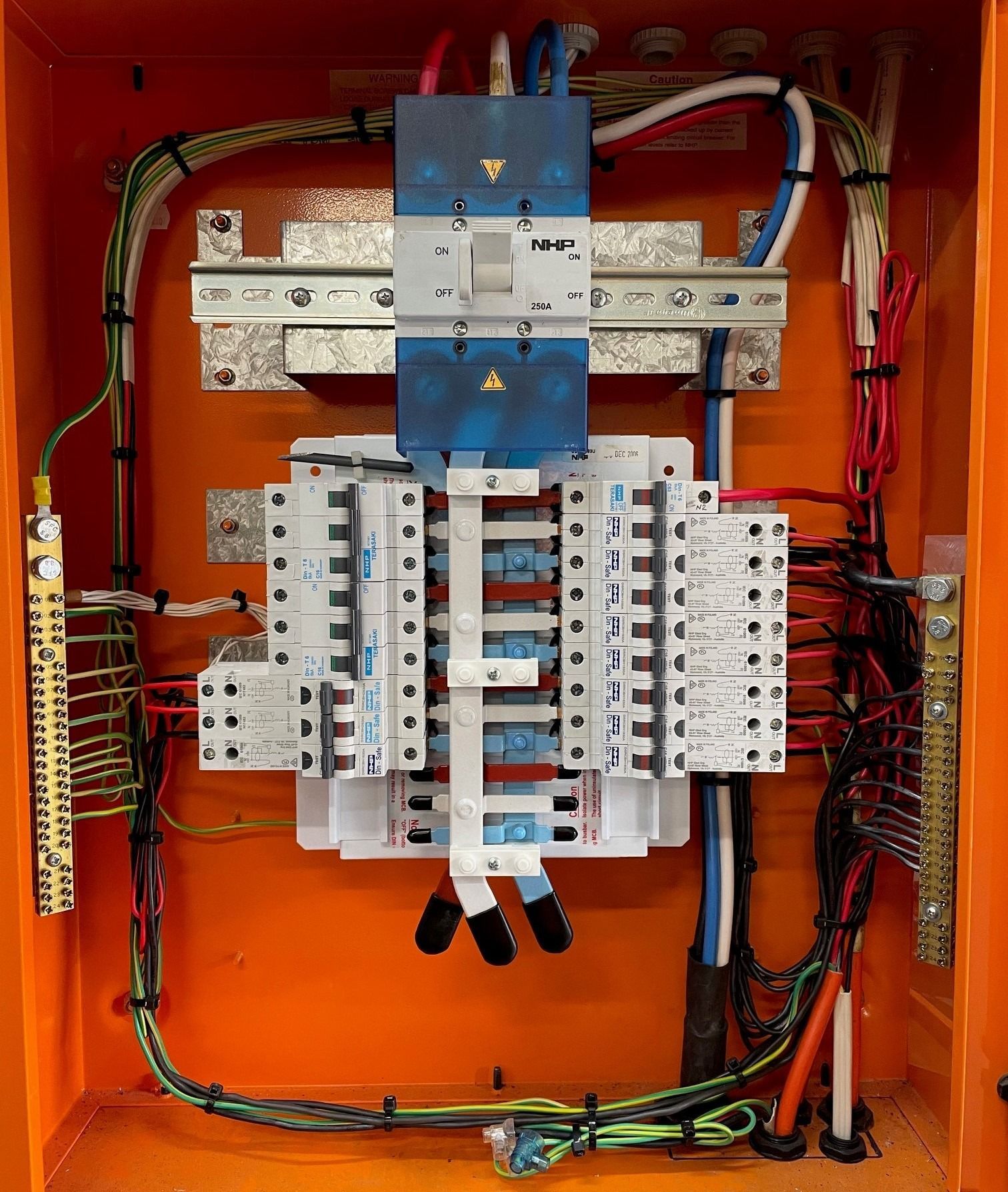 An electrical distribution board housed in an orange enclosure, featuring a main circuit breaker and multiple sub-breakers.