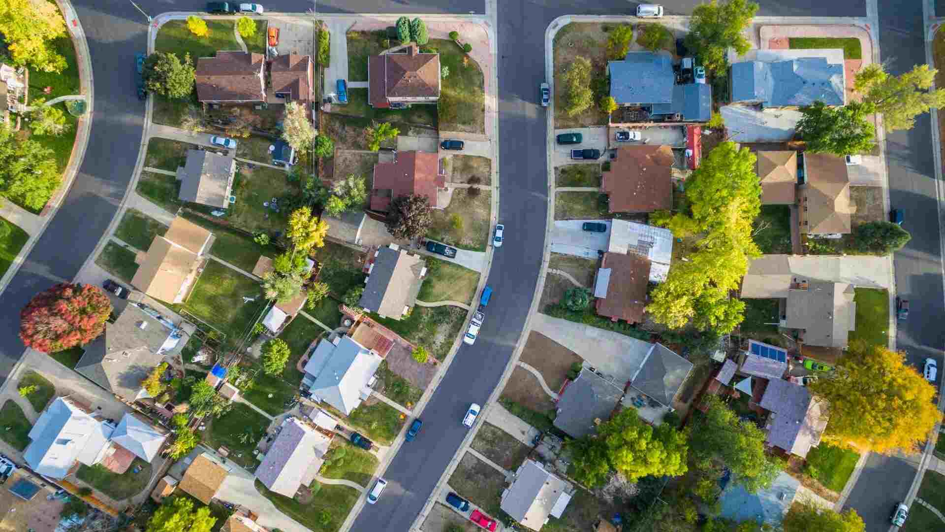 Bird’s eye view of a residential neighborhood with foliage, grass and cars parked around family-sized homes.