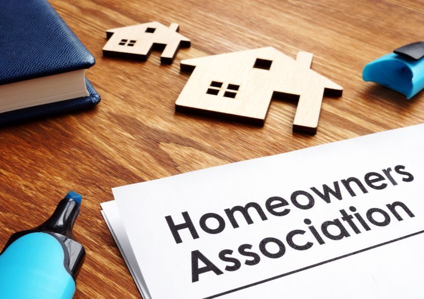 Two wooden carvings of houses are pictured on a hardwood desk over a paper document that reads ‘Homeowners Association’.