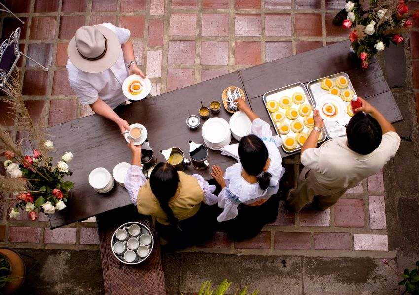 A bird’s eye view of a restaurant buffet is pictured, with three hospitality workers serving one guest coffee and breakfast food.