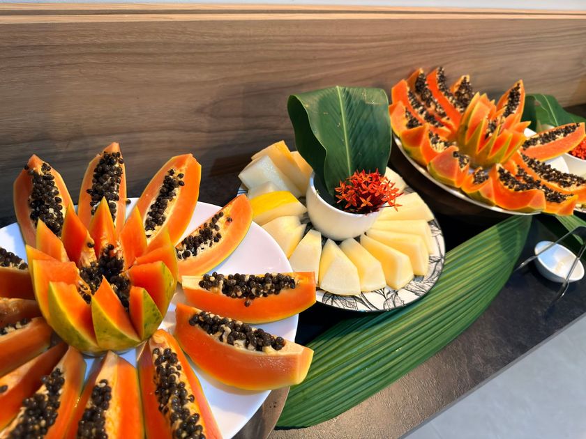 Pratos decorativos de frutas com mamão, abacaxi e melão esculpidos, dispostos sobre uma mesa.