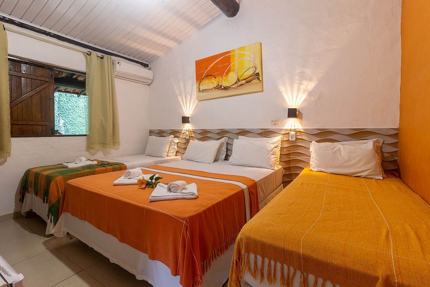 Quarto aconchegante com duas camas, roupa de cama laranja, abajures e janela com cortinas.
