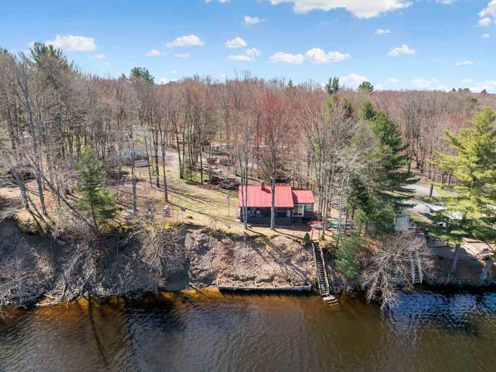 An aerial view of a house on the shore of a lake surrounded by trees.