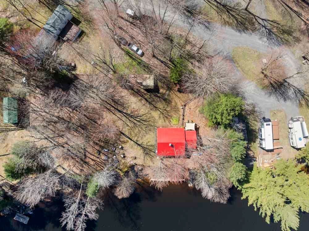 An aerial view of a red house surrounded by trees and a lake.