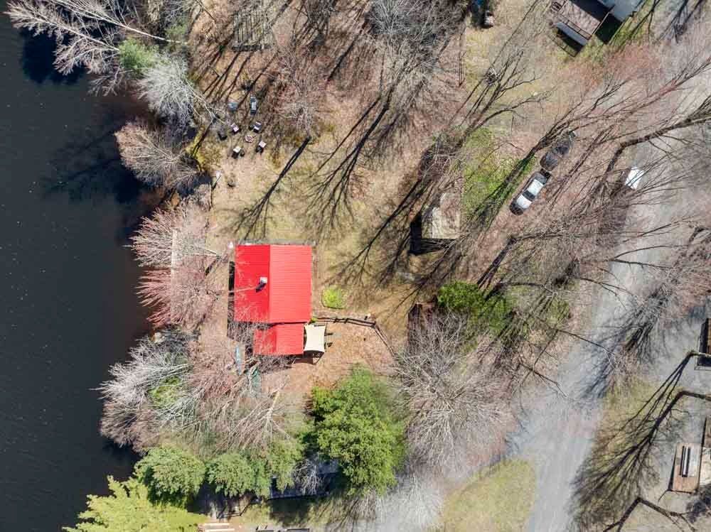 An aerial view of a house on a small island in the middle of a lake surrounded by trees.