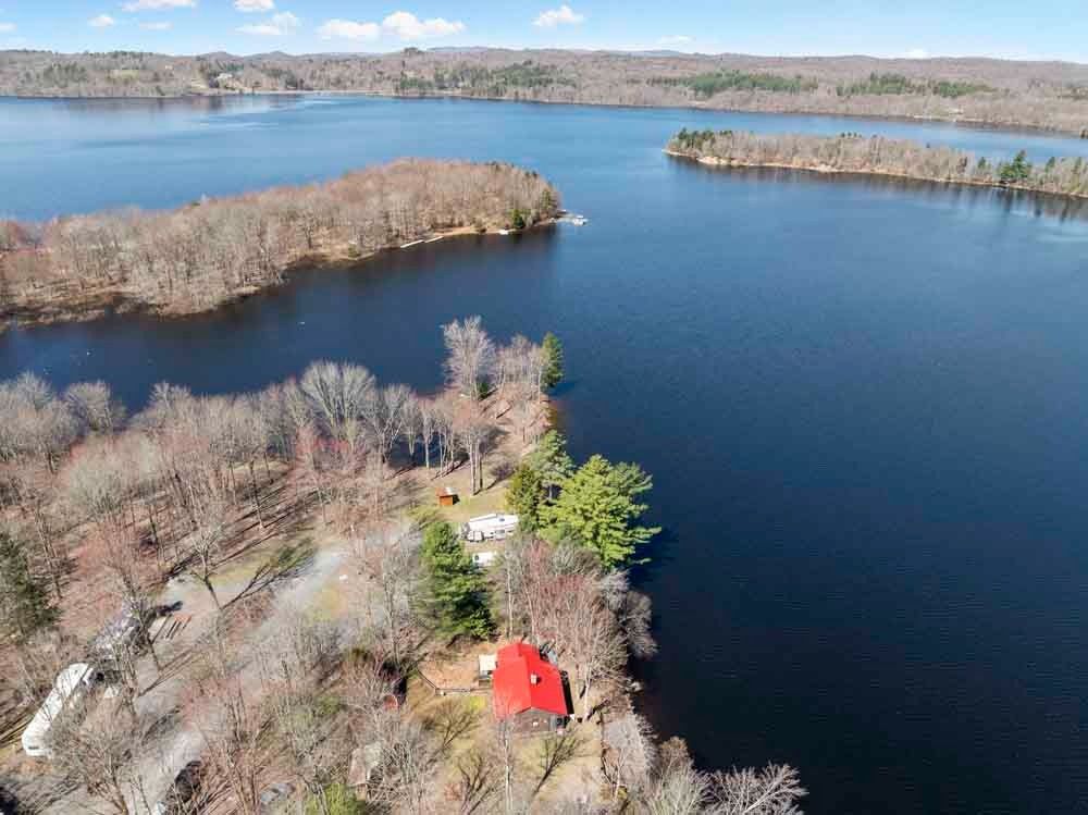 An aerial view of a house on the shore of a lake surrounded by trees.