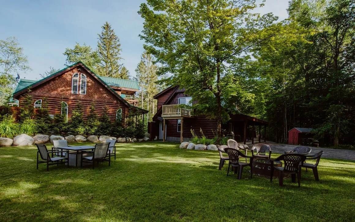 A large lawn with tables and chairs in front of a log cabin.