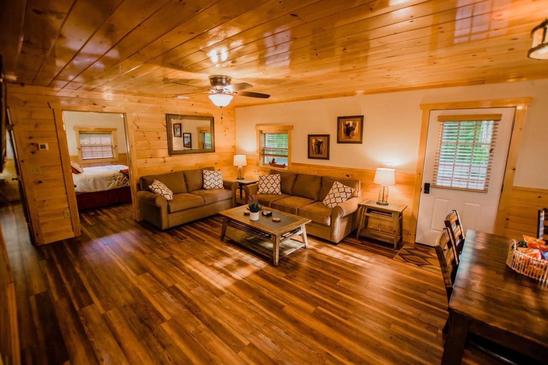 A living room in a cabin with a couch , table , chairs and a ceiling fan.