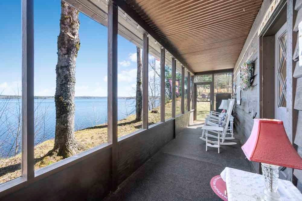 A screened in porch with rocking chairs and a lamp overlooking a lake.