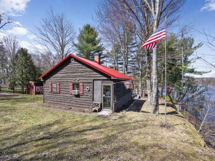 A small log cabin with a red roof is sitting next to a lake.